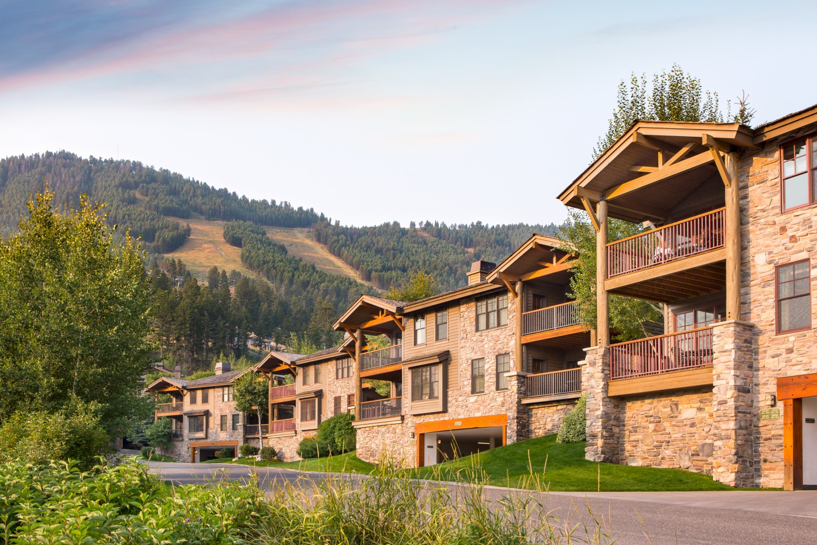 This image shows a row of multi-story houses with stone and wood exteriors, set against a backdrop of green mountains and a clear sky.