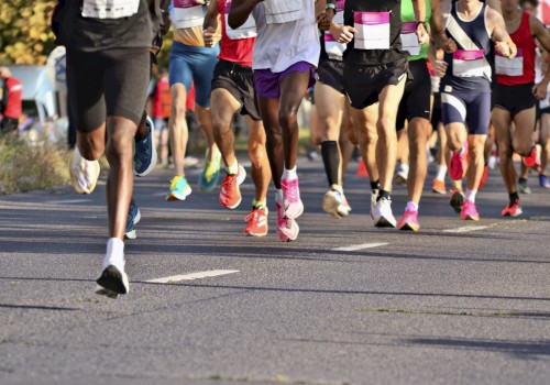 The image shows a group of runners participating in a road race, with focus on their legs and colorful shoes.