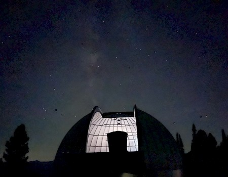 A silhouetted observatory dome under a starry night sky with trees visible in the background.