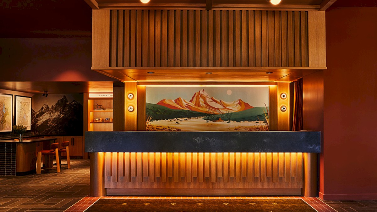 A warmly lit hotel reception area with wooden decor, a mountain painting, and seating in a cozy, inviting atmosphere.