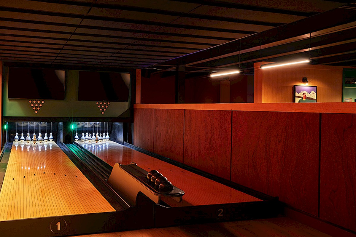 A bowling alley with two lanes, pins set up, scoring screens, and warm lighting inside a cozy entertainment venue.
