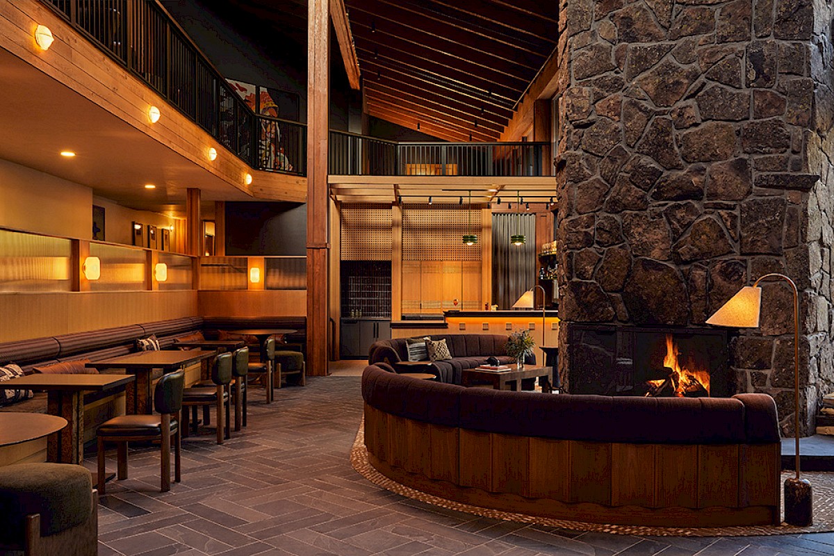 A cozy, modern lounge with a stone fireplace, inviting seating, warm lighting, and upstairs balcony in a rustic-inspired design.