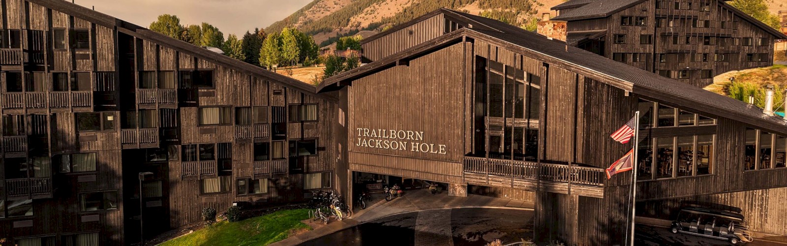 This image shows the Trailborn Jackson Hole lodge, a rustic wooden hotel with mountain scenery in the background.