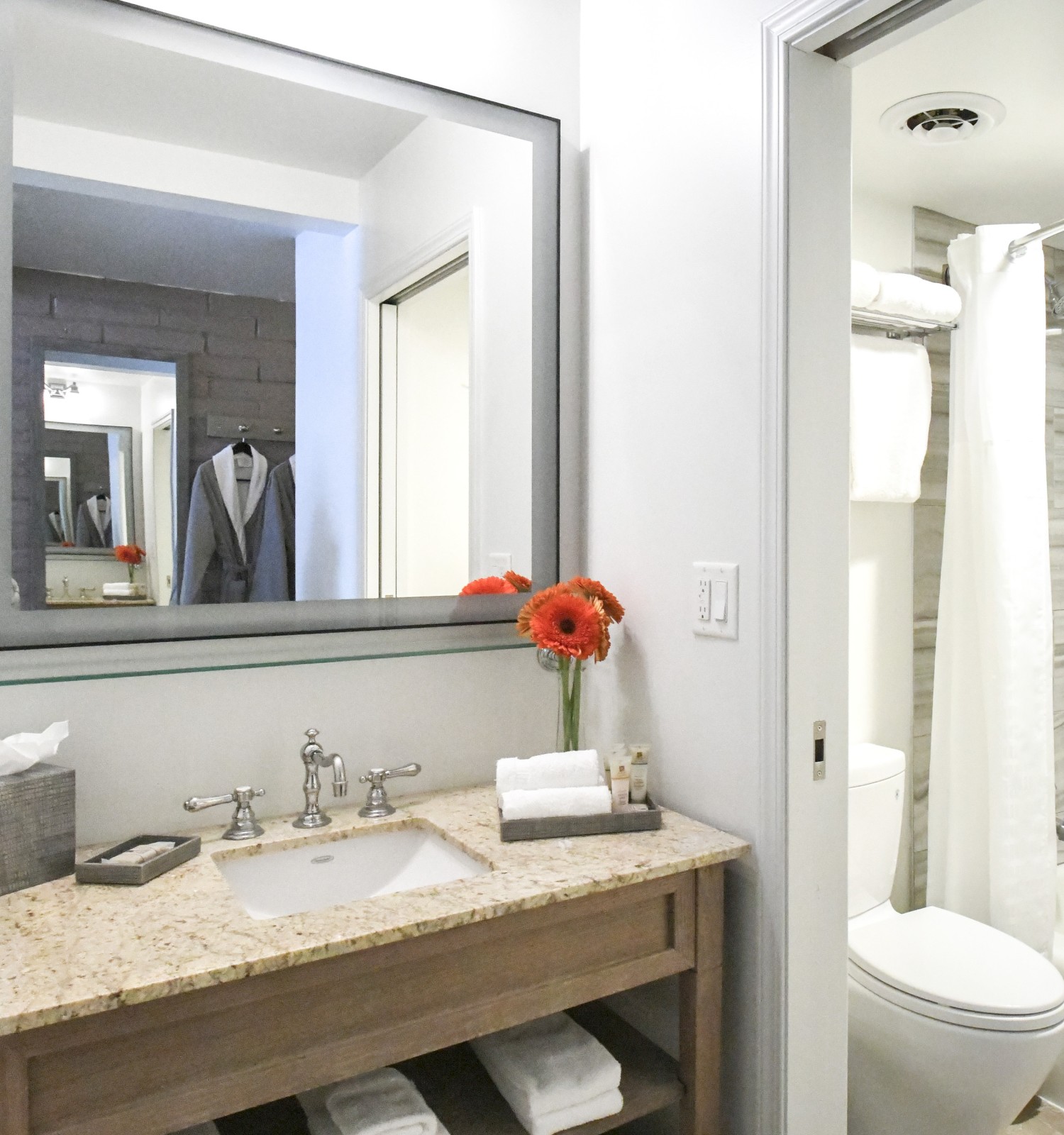 A modern bathroom with granite countertop, sink, mirror, red flowers, towels, bathtub, and shower curtain.